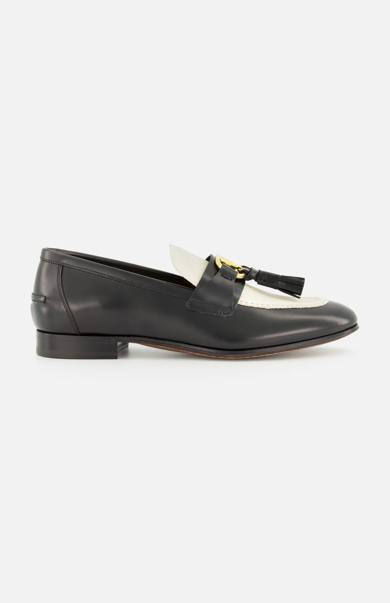 The Valentino Garavani Vaniteux Loafer by VALENTINO GARAVANI is a black and white women's leather loafer with a low heel, gold metal bit, and black tassel detail, offering classic slip-on elegance against a plain white background.