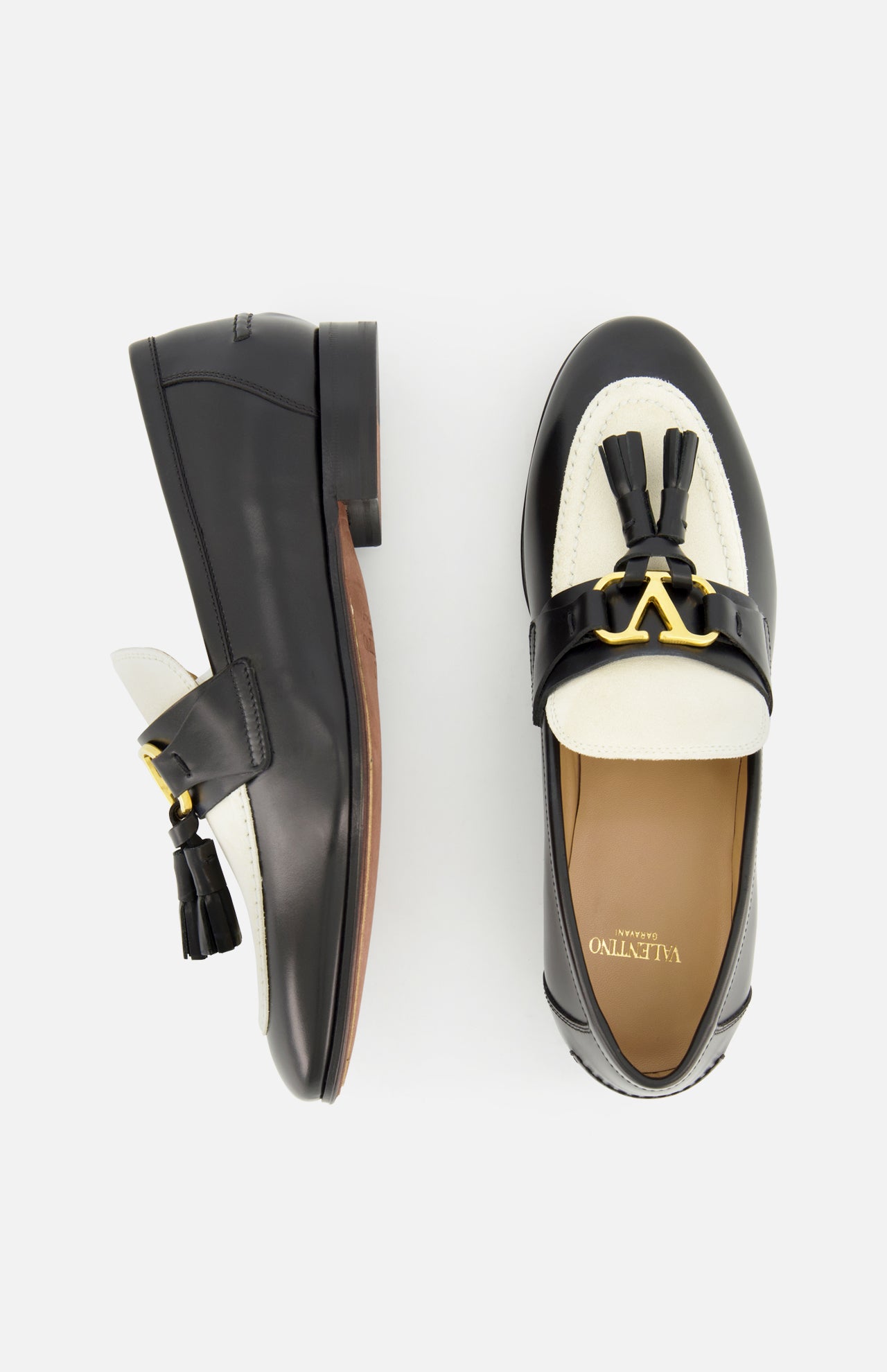 The VALENTINO GARAVANI Vaniteux Loafer is a women's black and white leather slip-on with tassels and gold hardware, featuring classic style and modern elegance, shown from side and top views on a white background.