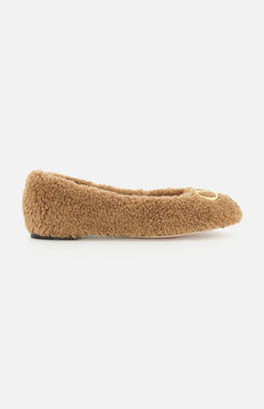The VLogo Signature Ballerina Flat by VALENTINO GARAVANI is displayed in a side profile view against a white background; this single brown fuzzy flat shoe features a rounded toe and is adorned with a gold circular embellishment near the front, evoking the cozy style of teddy bear ballet flats.