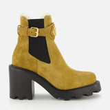 Introducing the VALENTINO GARAVANI VLogo Signature Beatle Boot: a mustard yellow suede ankle boot featuring a chunky black heel, rugged sole, side cutout, black elastic panel inspired by classic Chelsea boots in beige, gold buckle detail, and white shearling trim at the top.