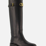 The VLogo Signature Boot by VALENTINO GARAVANI is a tall black leather equestrian boot featuring a low heel, gold buckle at the top, and a gold V logo detail on the outer side.