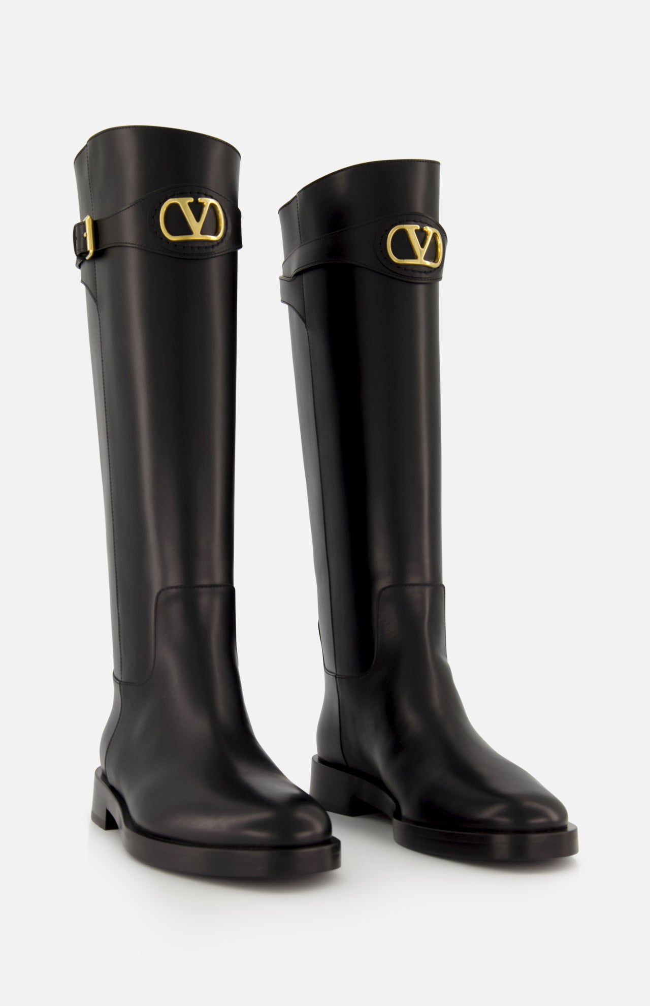The VALENTINO GARAVANI VLogo Signature Boot is a pair of knee-high black leather boots with low heels and gold “V” logo buckles near the cuffs, perfect for adding equestrian style to any outfit. Shown against a plain white background.