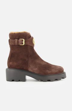 The VALENTINO GARAVANI VLogo Signature Sheepskin Bootie, featuring brown suede, a chunky black sole, luxurious sheepskin lining, and an elegant gold buckle, is showcased in side profile against a white background—an ideal fall choice for stylish comfort.