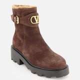 The VLogo Signature Sheepskin Bootie by VALENTINO GARAVANI features luxurious brown suede, a chunky black sole, a gold buckle, plush sheepskin lining for warmth, and the signature gold V logo on the side—making it the perfect addition to your fall boots collection.