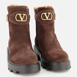 The VALENTINO GARAVANI VLogo Signature Sheepskin Bootie is a pair of brown suede ankle boots with chunky black soles, gold VLogo buckles, and light tan sheepskin lining at the tops—making these suede booties perfect for fall—shown against a plain white background.