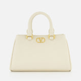 The VALENTINO GARAVANI VLogo Signature Mini Bag is an ivory bowling bag with two short handles, gold hardware, and a bold gold V logo on the front, shown against a plain white background.