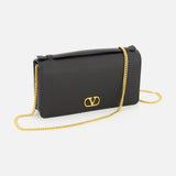 A VALENTINO GARAVANI VLogo Signature Wallet with Strap in black, featuring a rectangular shape, gold chain strap, and an eye-catching VLogo signature on the front, displayed against a white background.