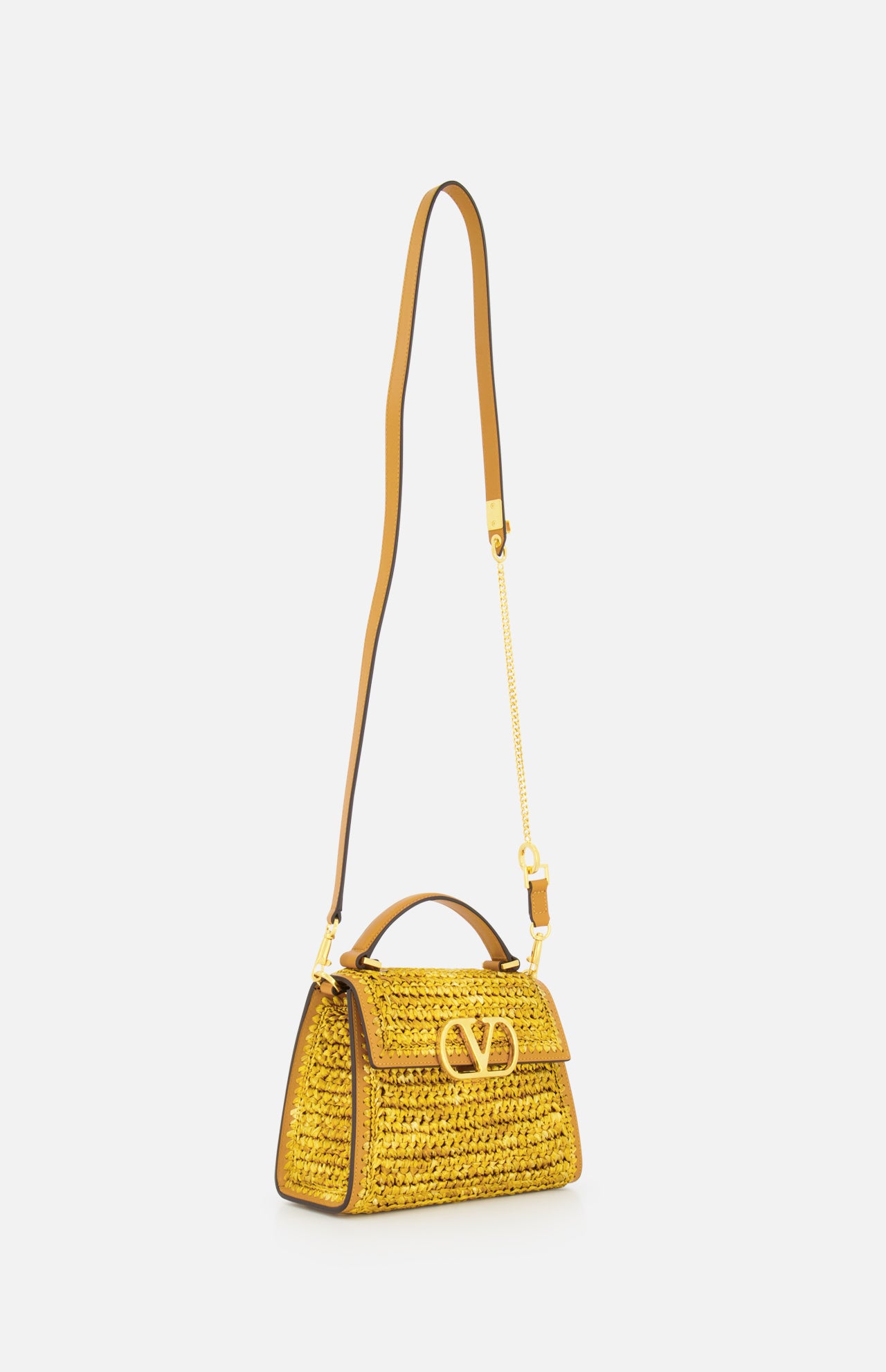 The VALENTINO GARAVANI VSling Small Top Handle Bag features yellow raffia-effect fabric, gold hardware, a gold “V” logo on the front flap, an adjustable leather shoulder strap, and is shown on a plain white background.