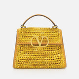 The VALENTINO GARAVANI VSling Small Top Handle Bag, made from yellow raffia-effect fabric with a prominent gold V logo on the front flap, is displayed against a plain white background.