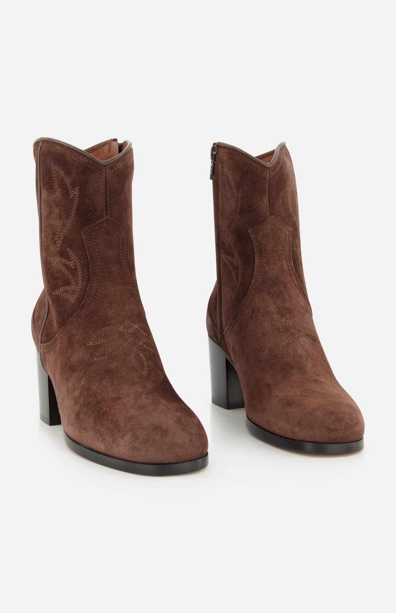 The Zimmy Western Bootie by VALENTINO GARAVANI features dark brown suede with decorative stitching, rounded toes, and chunky high heels. These boots are designed with side zippers and a subtle western-inspired look, offering a stylish update on classic western boots.