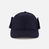 The Legacy Structured Merino Wool Earflap Hat by VARSITY HEADWEAR is shown from the front, featuring dark blue wool, side earflaps, and an adjustable back strap. The cap is photographed against a plain light gray background.