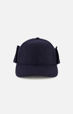 The Legacy Structured Merino Wool Earflap Hat by VARSITY HEADWEAR is shown from the front, featuring dark blue wool, side earflaps, and an adjustable back strap. The cap is photographed against a plain light gray background.