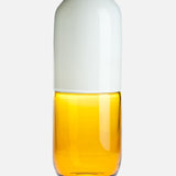 The VENINI Happy Pill Oxytocin Decor features a glass container with a white, rounded cap and transparent amber-yellow base, inspired by Murano glass artistry, shown against a plain white background.