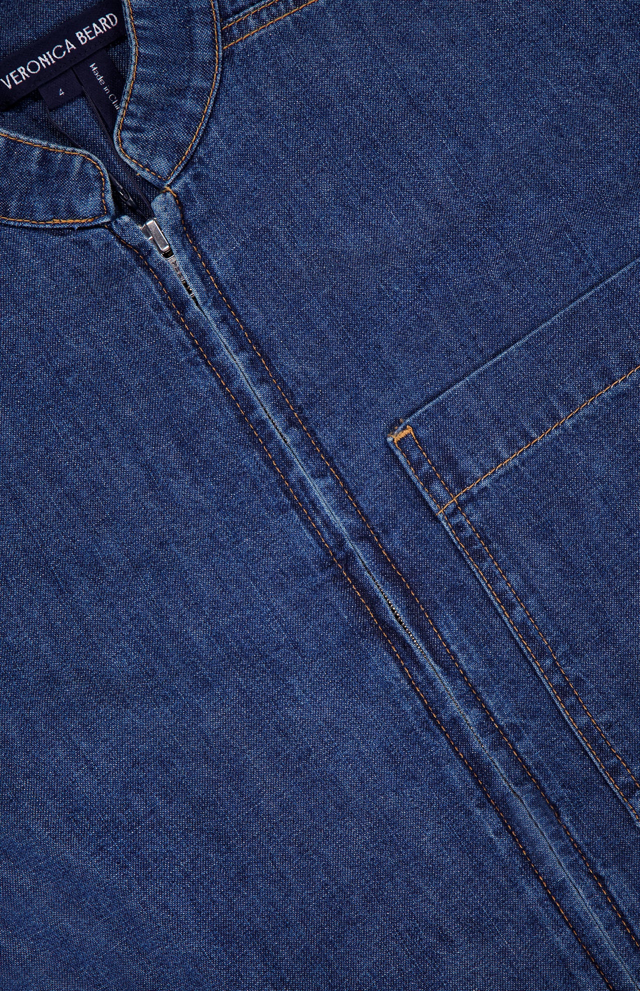 Close-up of the Akerman Denim Mini Dress by VERONICA BEARD, featuring a visible zipper, chest pocket, brown stitching, and a partial VERONICA BEARD label at the neckline.