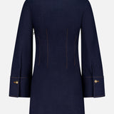The Raymond Denim Mini Dress by VERONICA BEARD is shown from the back on a white background. This dark blue dress features long sleeves, wide cuffs, gold buttons, and visible tan stitching for a modern, structured look.