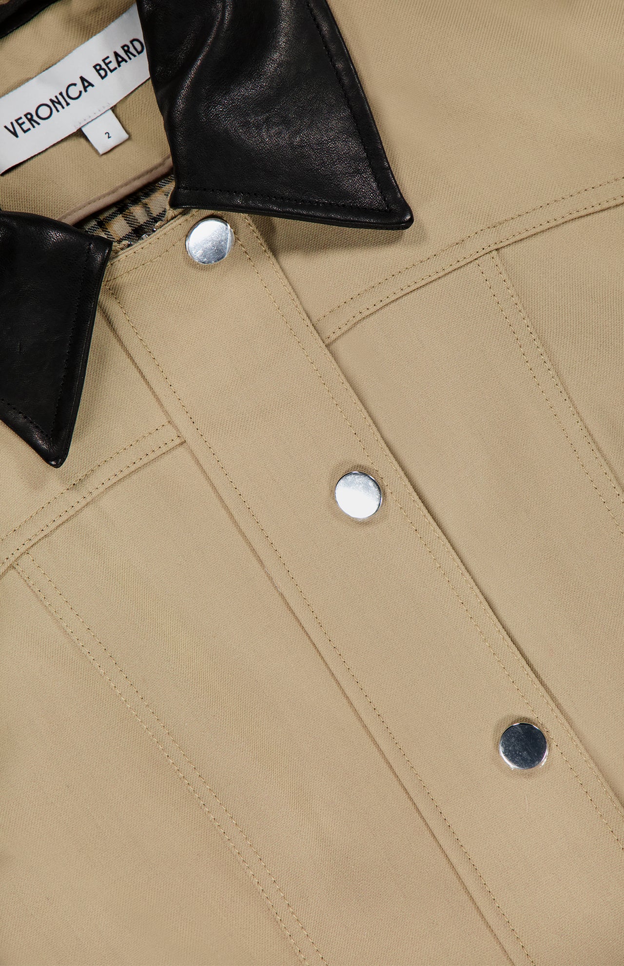 Close-up of the VERONICA BEARD Talla Water Repellant Jacket in khaki, featuring silver snap buttons, a black leather collar, and a visible brand label inside the neckline.