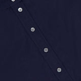 Close-up of the Aleck Scalloped Embroidery Shirt by VERONICA BEARD, a navy boxy blouse with a round neckline and six silver buttons down the front. A white collar tag partially shows the brand name.