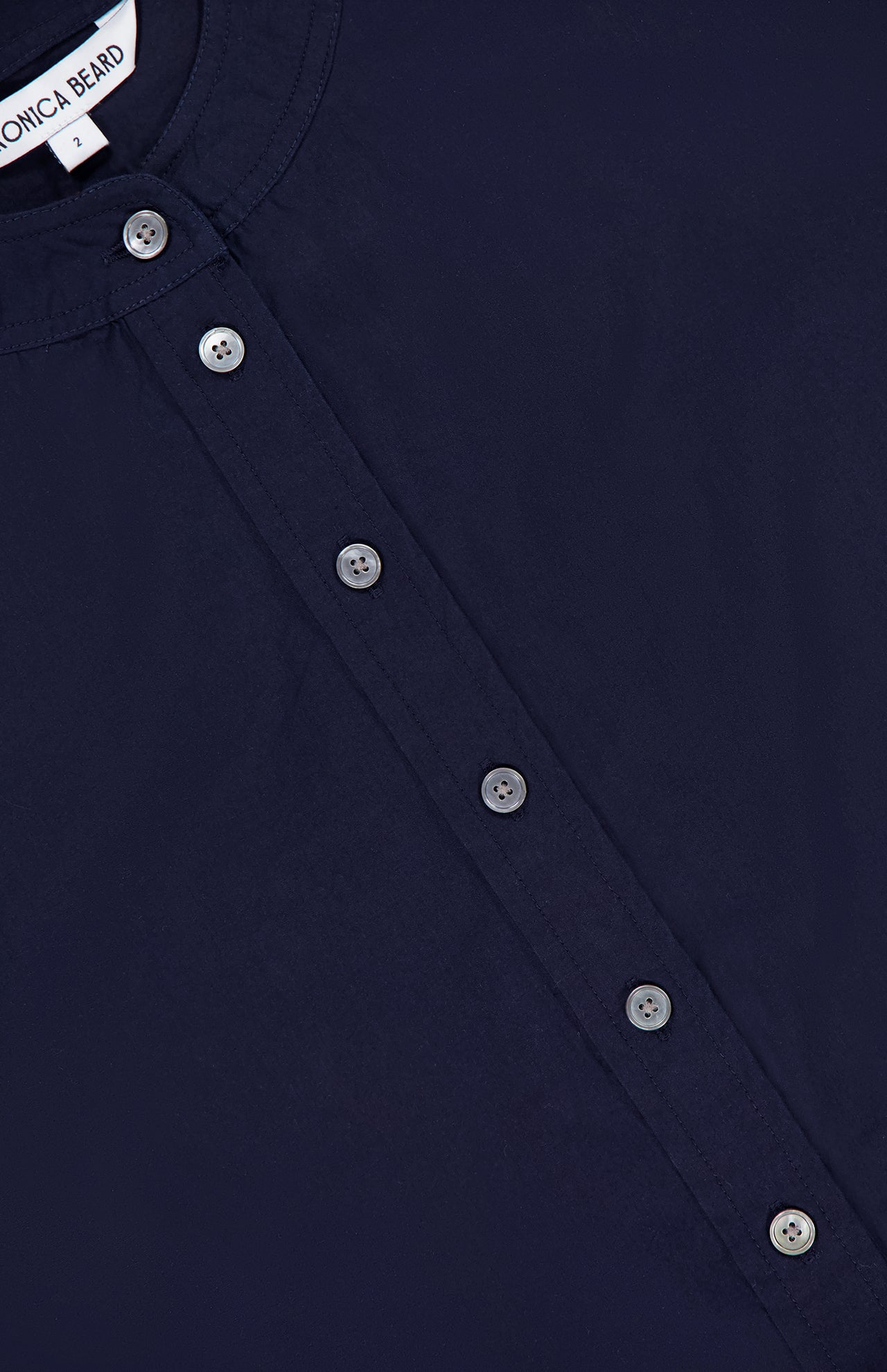 Close-up of the Aleck Scalloped Embroidery Shirt by VERONICA BEARD, a navy boxy blouse with a round neckline and six silver buttons down the front. A white collar tag partially shows the brand name.
