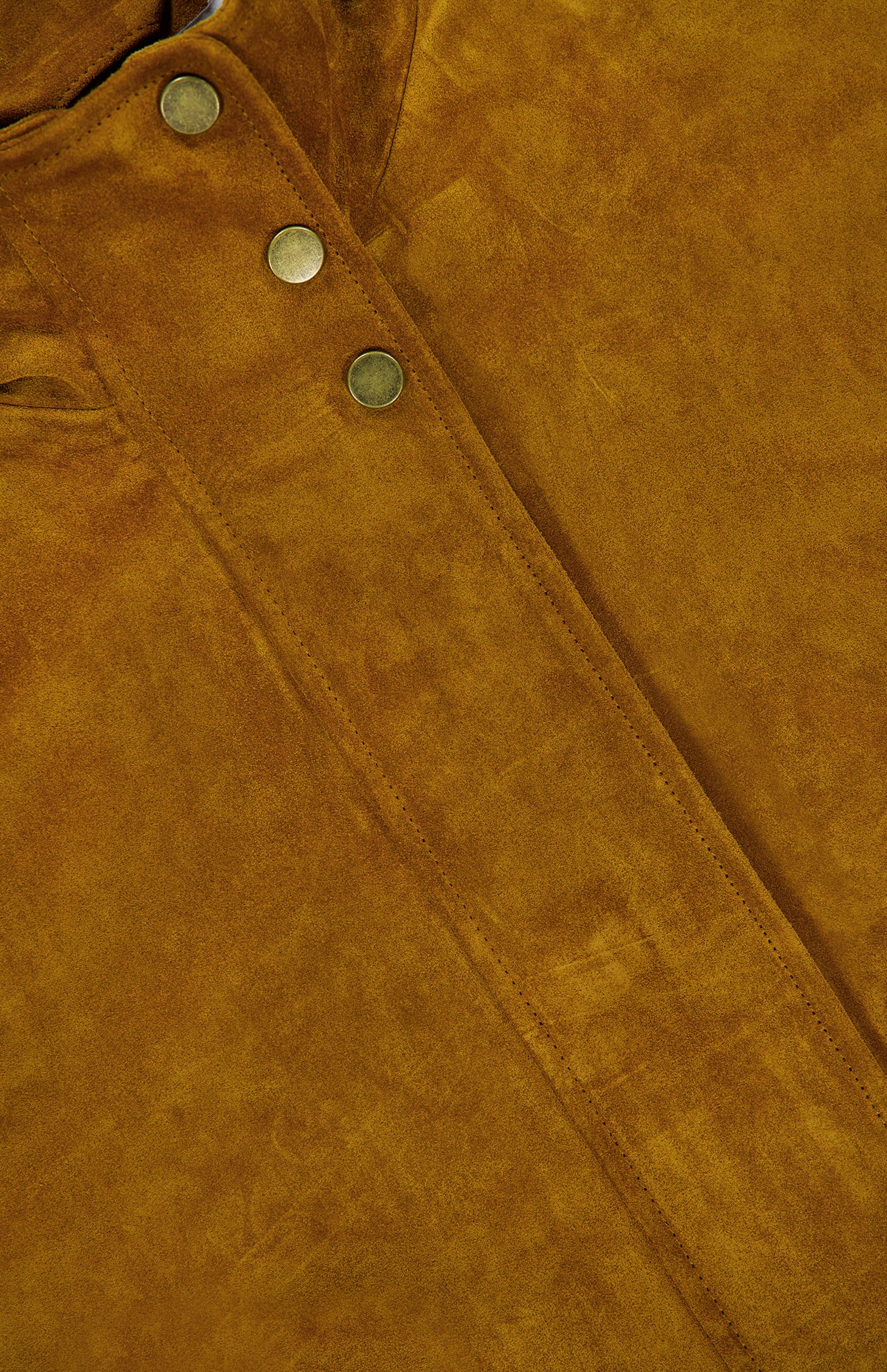 Close-up of brown suede fabric with a seam and three metallic snap buttons, highlighting the texture and rich color of the material—showcasing the perfect details of the Bateman Cropped Suede Jacket by VERONICA BEARD, ideal as fall outerwear.