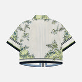 The Clean Spruce Cropped Top by VERONICA BEARD is a short-sleeved, boxy fit shirt in light cream with green and blue botanical print, featuring black and white striped trim on the sleeves and hem. Back view shown.