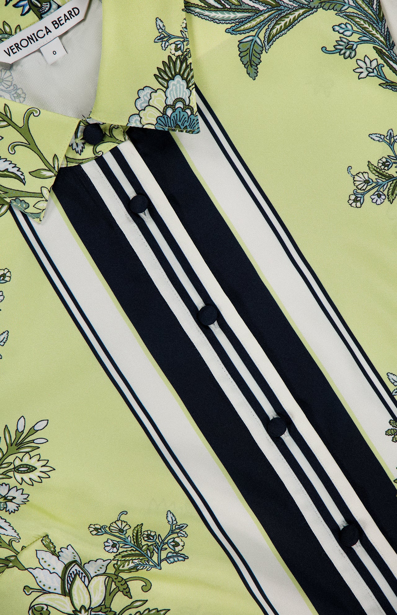 Close-up of the Clean Spruce Cropped Top by VERONICA BEARD: light green, cropped, with black buttons, floral designs on the collar and parts, plus black and white vertical stripes. Brand label is visible inside the collar.