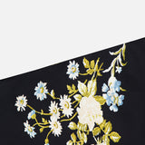 The Clover Floral Midi Skirt by VERONICA BEARD features a diagonal section of black stretch georgette fabric adorned with a floral pattern of white and blue flowers with green leaves, set against a plain white background.