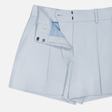 The Craig High Rise Short by VERONICA BEARD in light blue Italian cotton-blend twill features pleats, belt loops, a white inner waistband button, metal hooks, and zip closure, shown partially unbuttoned and unzipped.
