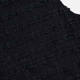 Close-up of the VERONICA BEARD Ruffled Cropped Jordyn Tank, a sleeveless black top crafted from textured stretch jersey with horizontal micro-ruffles. A navy blue label with white text appears at the neckline.