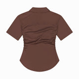 The Devra Short Sleeve Ruched Top by VERONICA BEARD is a brown stretch cotton poplin shirt, seen from the back, featuring waist-defining ruching and a slightly curved hem for a fitted silhouette.