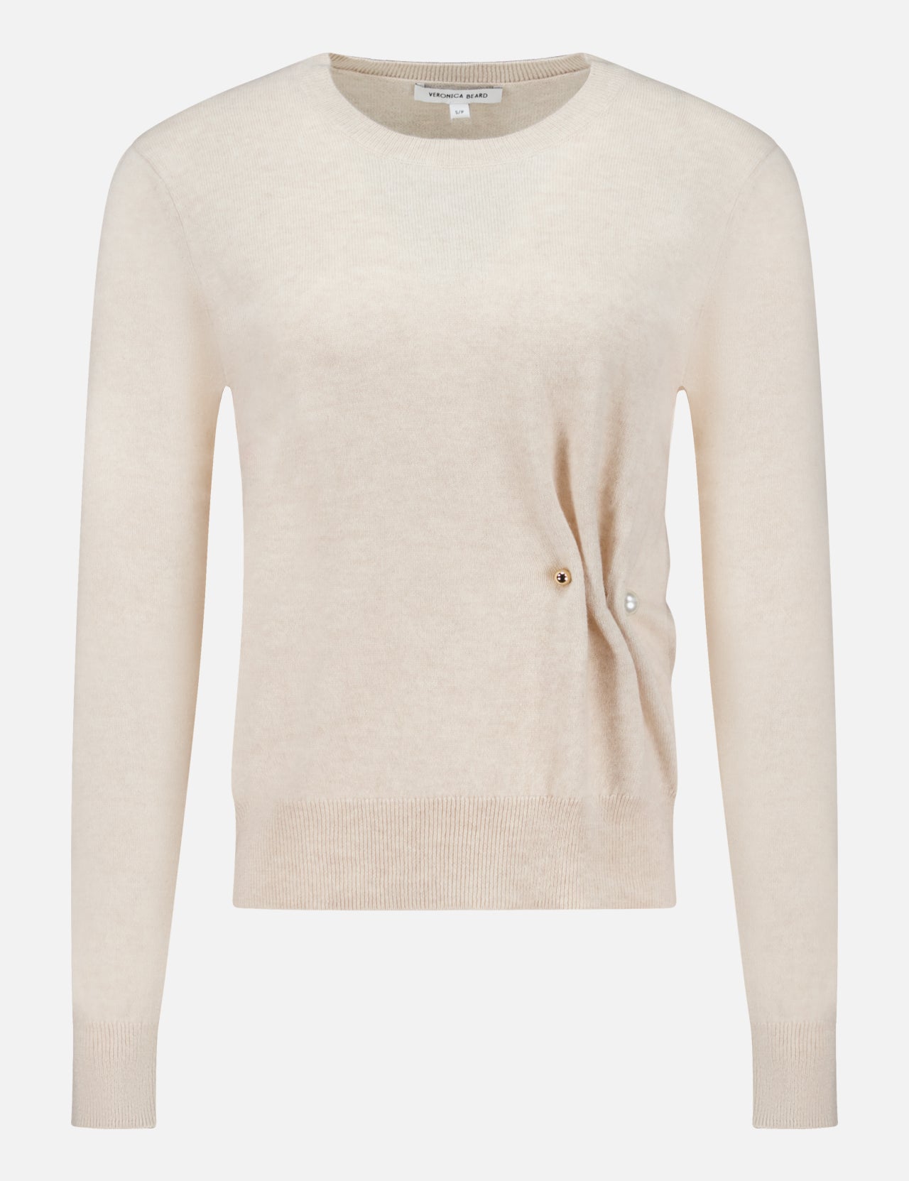 The Frankie Pearl Pin Pullover Sweater by VERONICA BEARD is a long-sleeved, light beige neutral sweater with a round neckline. Crafted from soft merino wool, it features a subtle ribbed hem and cuffs, along with a distinctive small pearl pin detail on the right side near the waist, offering both comfort and timeless elegance.
