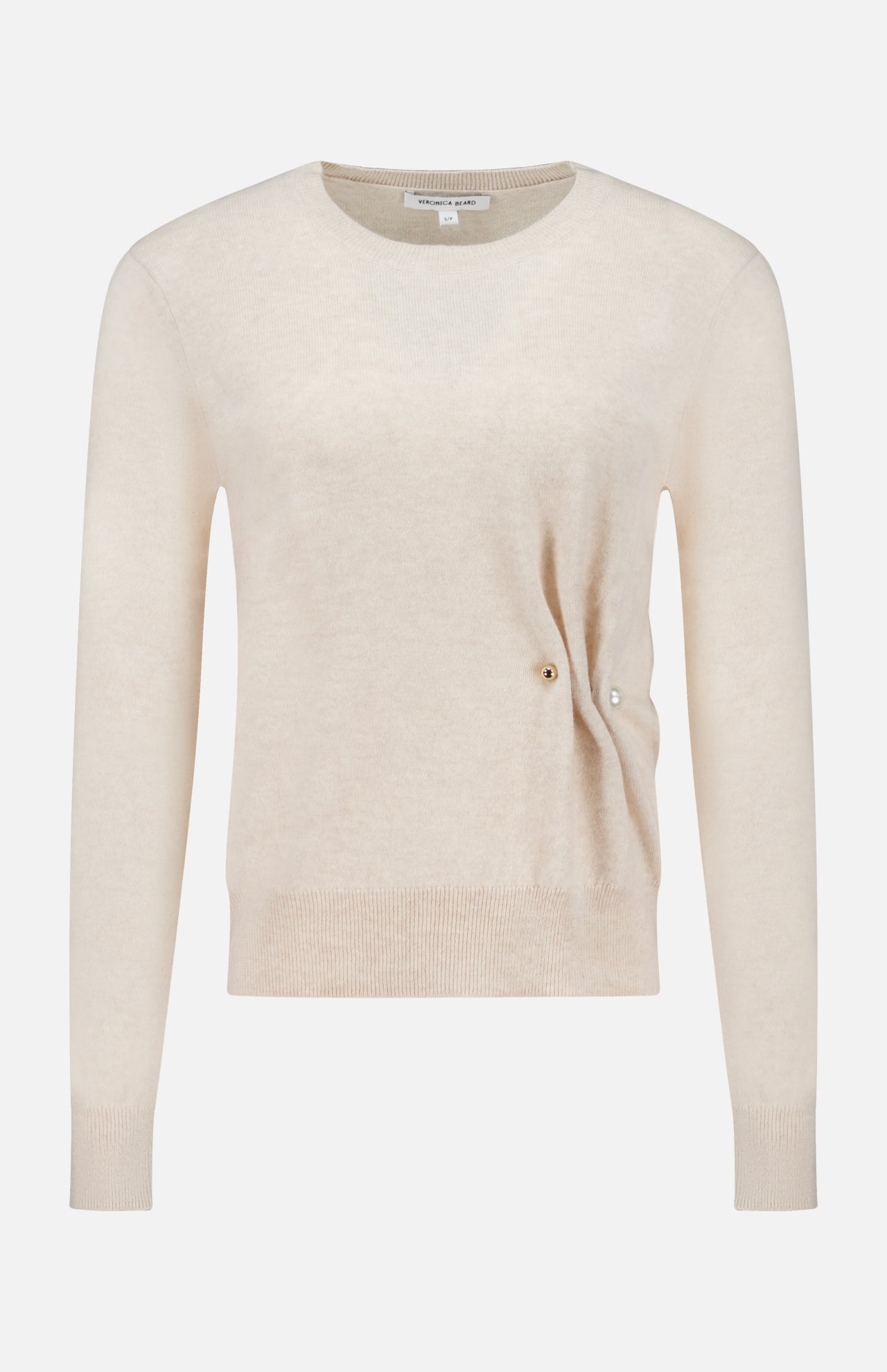 The Frankie Pearl Pin Pullover Sweater by VERONICA BEARD is a long-sleeved, light beige neutral sweater with a round neckline. Crafted from soft merino wool, it features a subtle ribbed hem and cuffs, along with a distinctive small pearl pin detail on the right side near the waist, offering both comfort and timeless elegance.