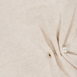 Close-up of the Frankie Pearl Pin Pullover Sweater by VERONICA BEARD, featuring light beige merino wool fabric with a gold button and a pearl pin detail creating a small gathered fold.