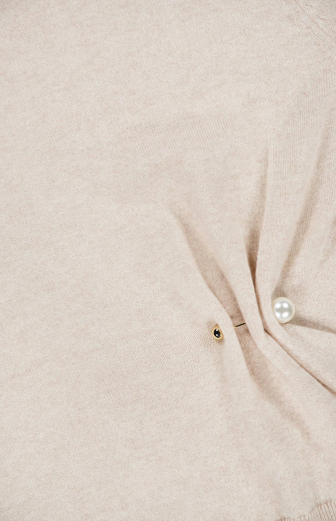 Close-up of the Frankie Pearl Pin Pullover Sweater by VERONICA BEARD, featuring light beige merino wool fabric with a gold button and a pearl pin detail creating a small gathered fold.