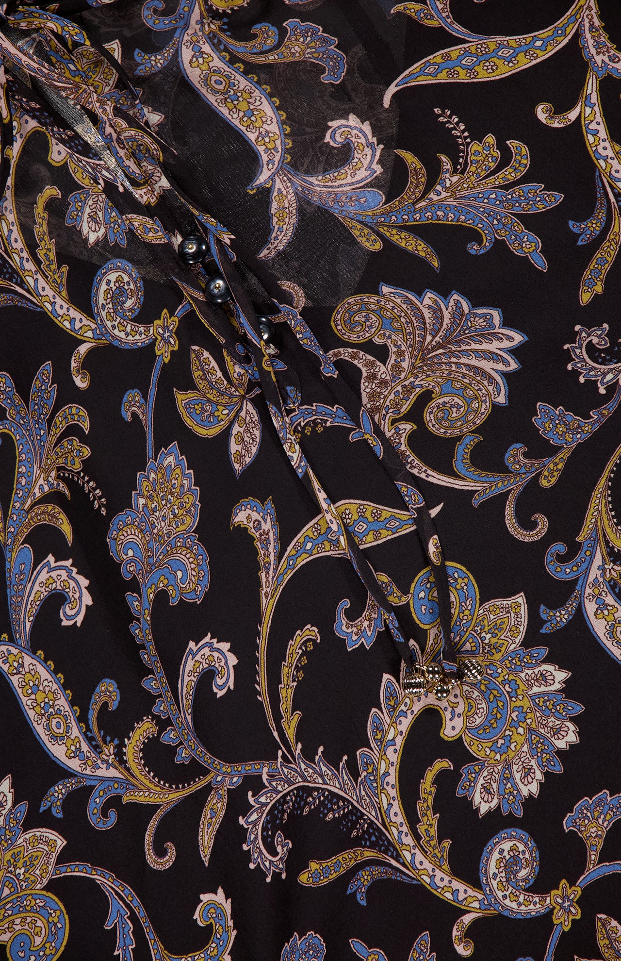 The VERONICA BEARD Silk Hickory Blouse showcases black silk georgette with blue, yellow, and beige paisley patterns, decorative swirls, leaf motifs, buttons, and a sheer overlay for a chic bohemian vibe.