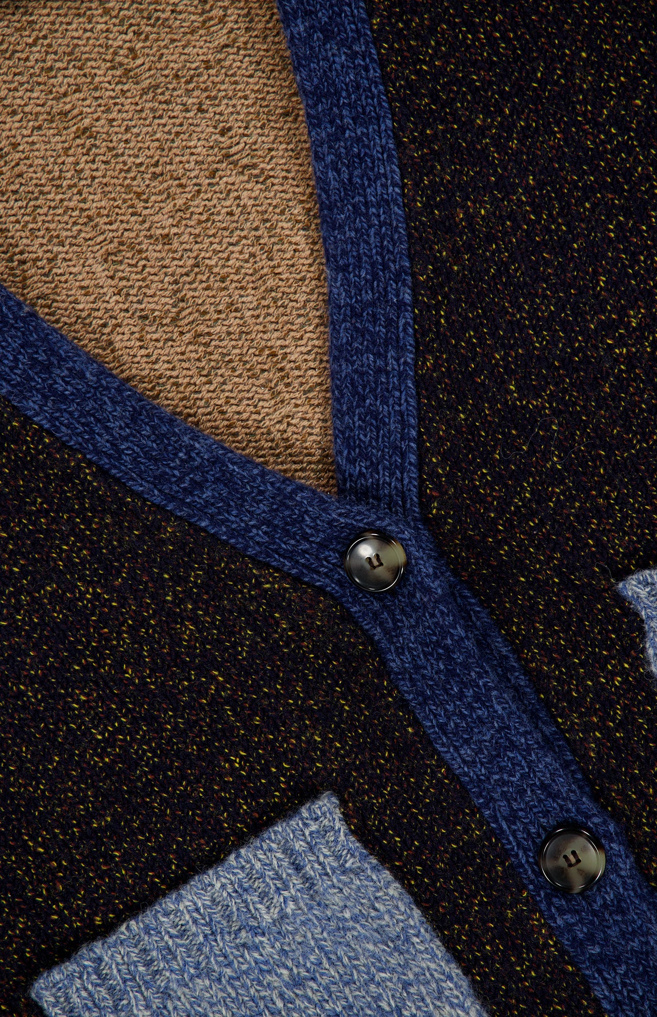 Close-up of the Josiane Cardigan Sweater from VERONICA BEARD’s knitwear collection, showcasing black and brown fabric with blue trim, two buttons, and a patch of light blue knit material for a modern colorblock effect.