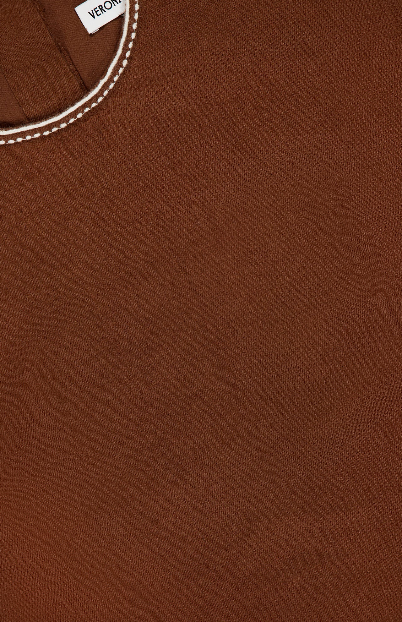 Close-up of the Kessan Embroidered Linen Top by VERONICA BEARD, featuring brown fabric with white stitching detail along the neckline and a small visible clothing tag.