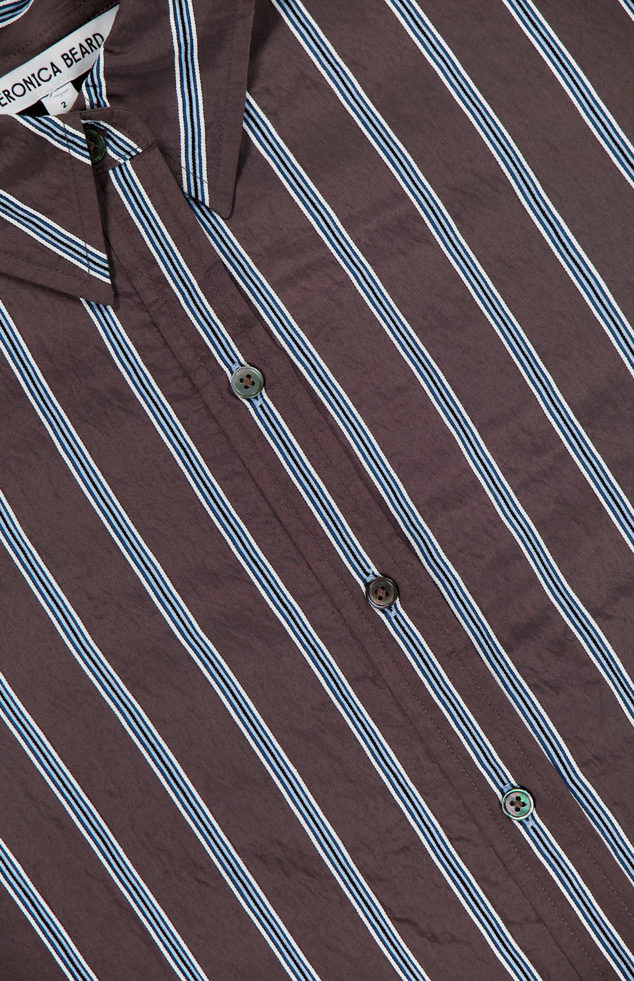 Close-up of the VERONICA BEARD Lloyd Striped Button Down Shirt, showcasing brown fabric with white and blue vertical stripes, a visible collar, and relaxed fit.