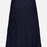 The Massimo Stretch Midi Skirt by VERONICA BEARD is an A-line navy midi skirt with crinkled textured fabric, ideal for transitioning from office to evening. Displayed on a plain white background.