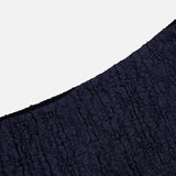A close-up of the dark blue, crinkled fabric and black edge from the Massimo Stretch Midi Skirt by VERONICA BEARD, shown against a plain white background.