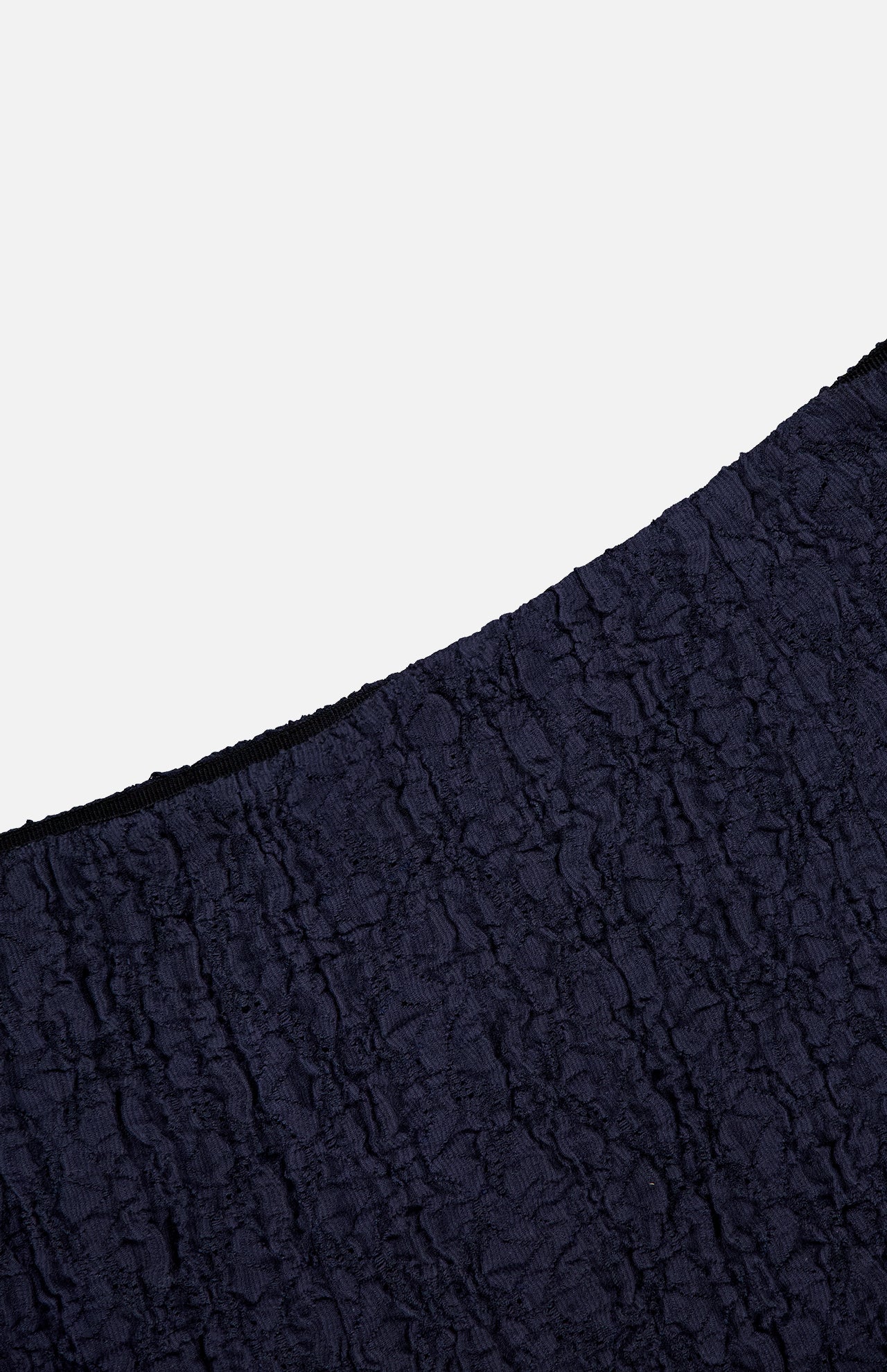 A close-up of the dark blue, crinkled fabric and black edge from the Massimo Stretch Midi Skirt by VERONICA BEARD, shown against a plain white background.