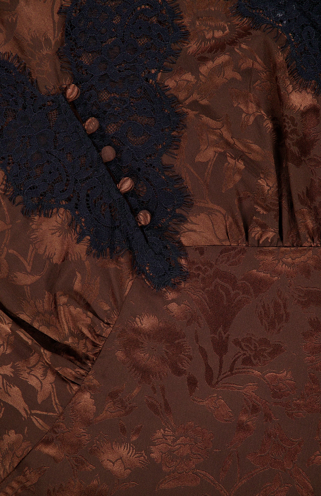 Close-up of the Pascaline Floral Lace Top by VERONICA BEARD, showcasing brown jacquard fabric with a floral motif, black lace trim, and brown decorative buttons arranged vertically.