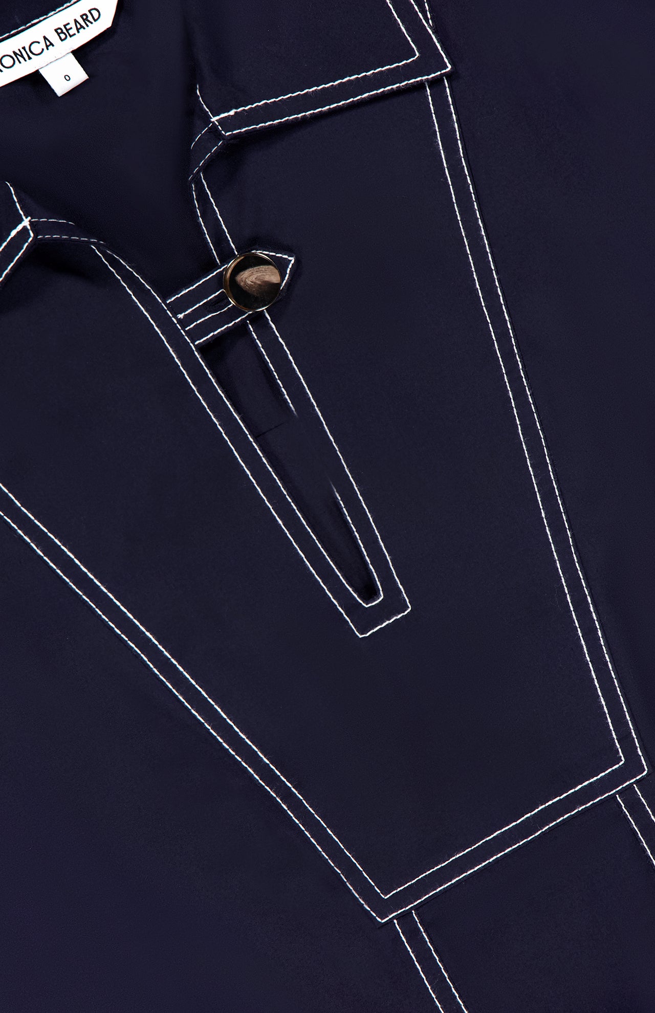 Close-up of the Phelix Topstitched Mini Dress by VERONICA BEARD, featuring dark navy stretch-cotton poplin, white contrast stitching, a pointed collar, geometric front design, neckline button detail, and a relaxed fit.