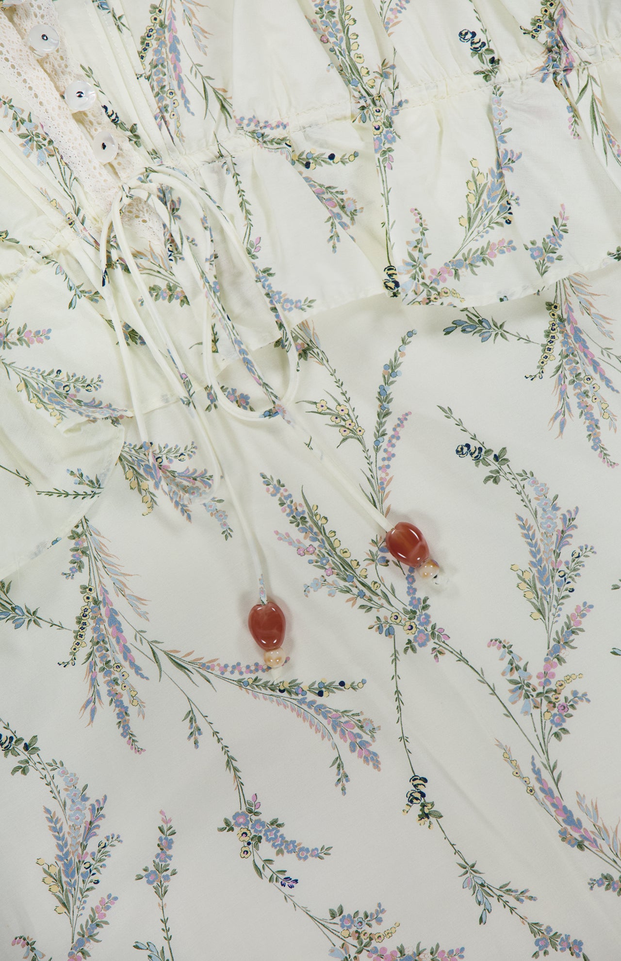 A close-up of the VERONICA BEARD Sleeveless Dominick Prairie Floral Dress shows light cotton-silk voile with pastel floral print, featuring two drawstrings with heart-shaped beads and lace trim.
