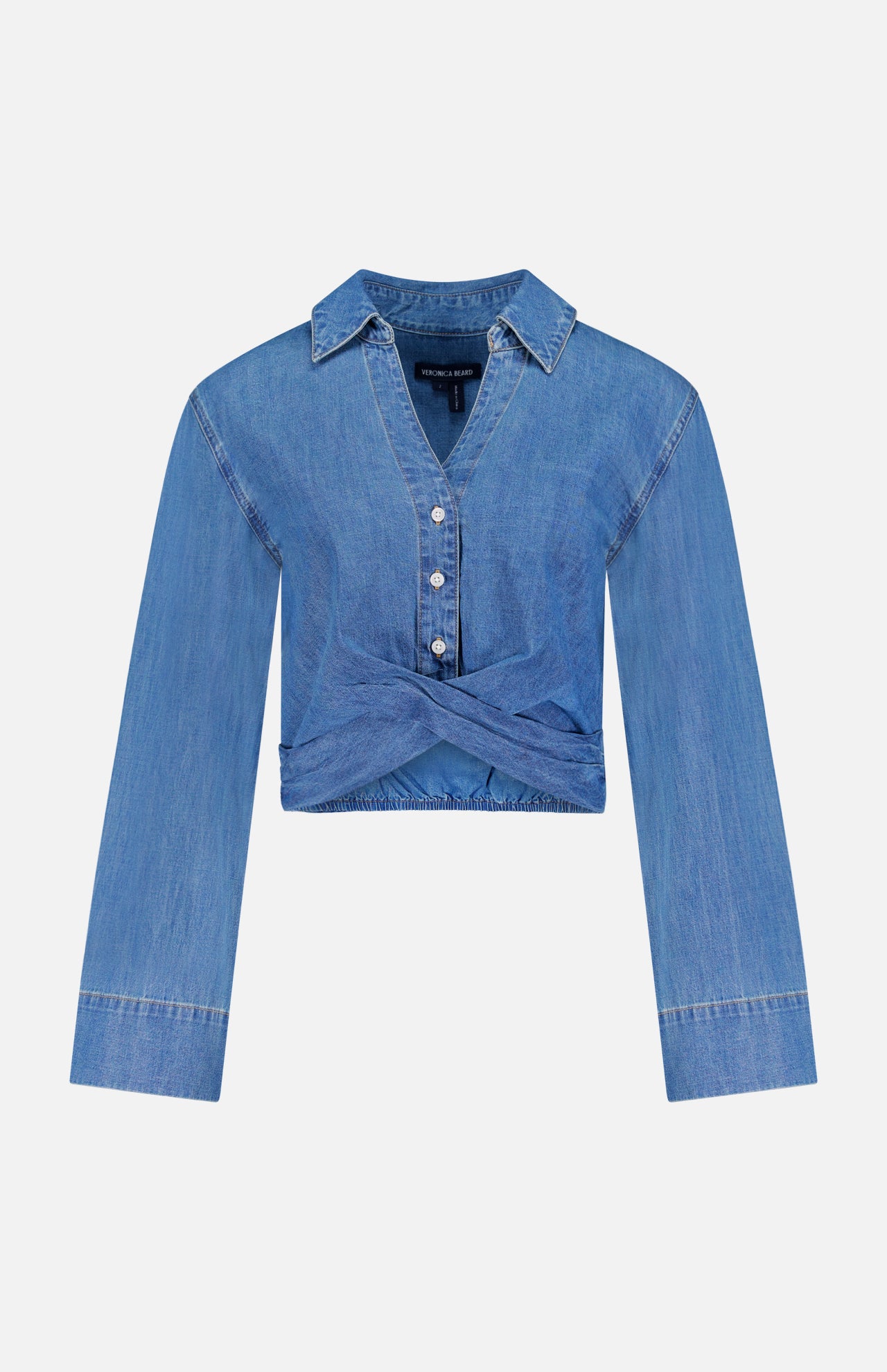 The Timothy Twist Detail Shirt by VERONICA BEARD is a long-sleeve, light blue cropped denim shirt with a collared neckline, button-down front, and twist waist detail, shown on a plain white background.