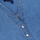 Close-up of the Timothy Twist Detail Shirt by VERONICA BEARD—a blue jean shirt with light brown stitching, white buttons, label inside the collar, and a subtle twist waist detail.