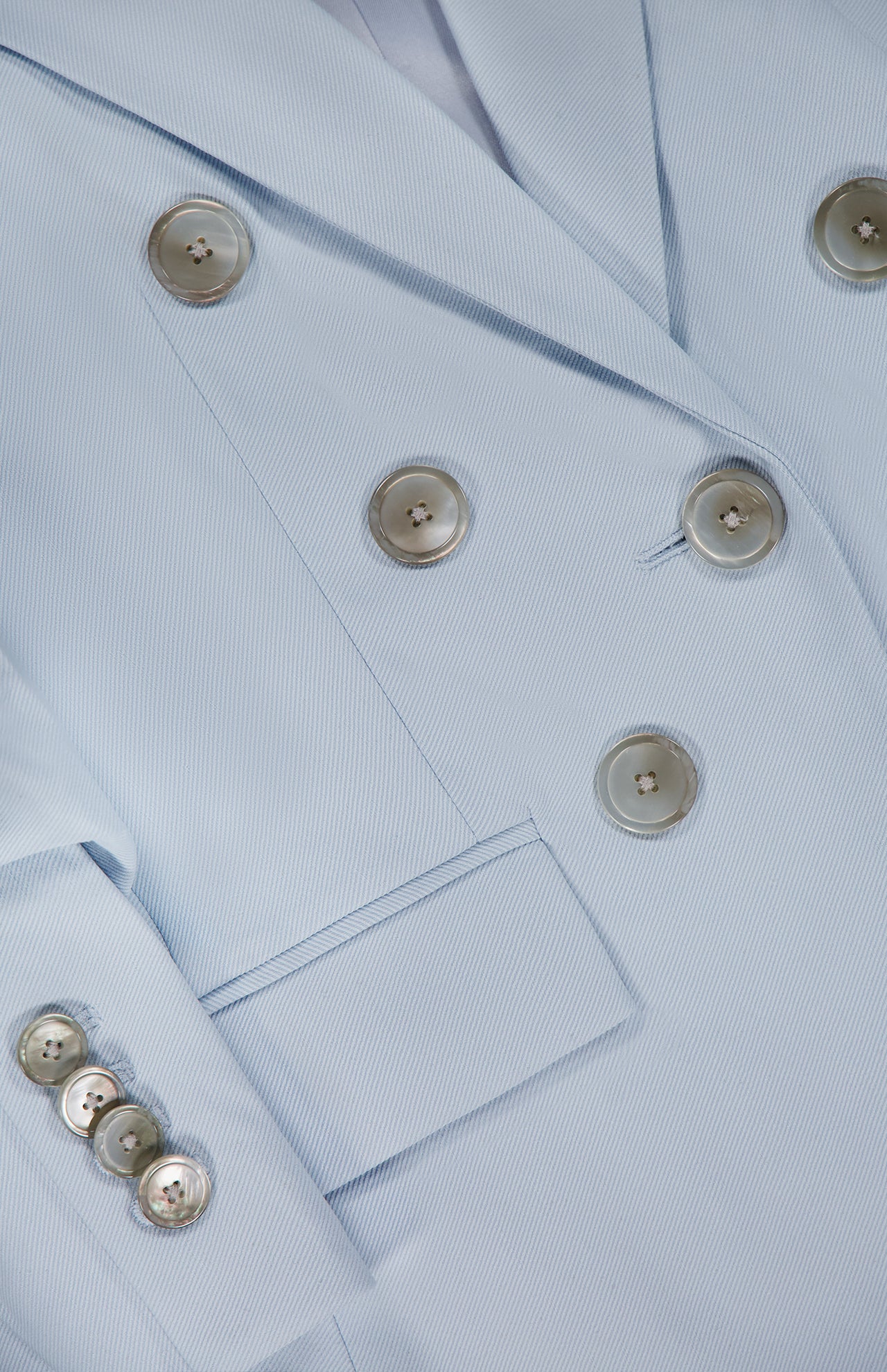 Close-up of the Tomi Dickey Jacket by VERONICA BEARD, in pale blue Italian twill. Features metallic buttons, a front pocket, textured fabric, and is dickey compatible for versatile styling.