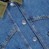Close-up of the Wegner Double Collar Denim Jacket by VERONICA BEARD, showcasing its blue denim fabric with a distinctive green corduroy collar, silver snap buttons, visible pockets, and brown stitching—this stylish jacket puts a modern spin on the classic jean style with its unique double collar design.