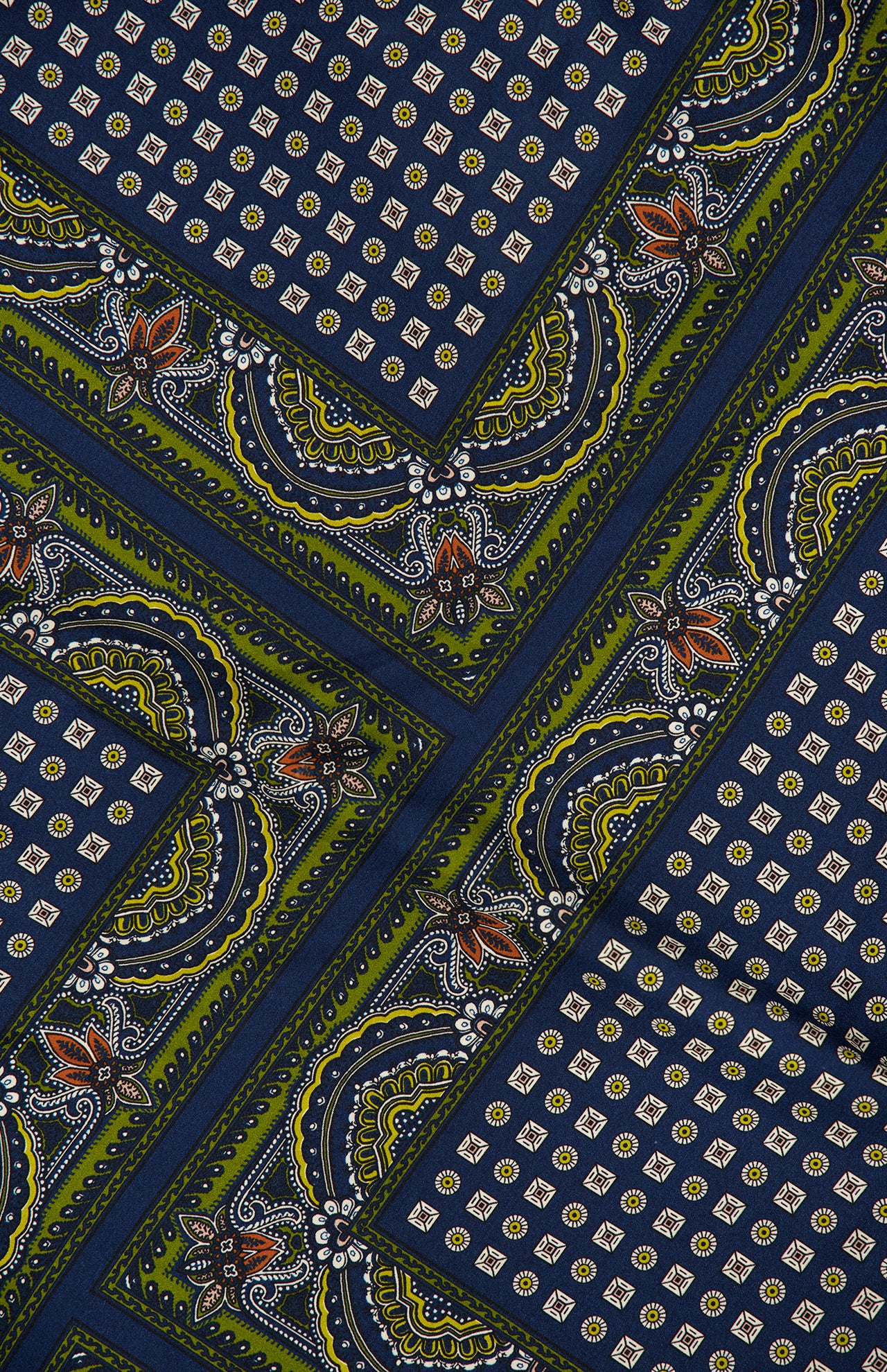 The Yvonne Scarf Print Top by VERONICA BEARD features colorful fabric adorned with diagonal green and blue stripes, small gold dots, and intricate paisley and floral patterns in orange, white, and black, creating a vibrant geometric design reminiscent of a luxurious scarf print or an asymmetrical silk blouse.