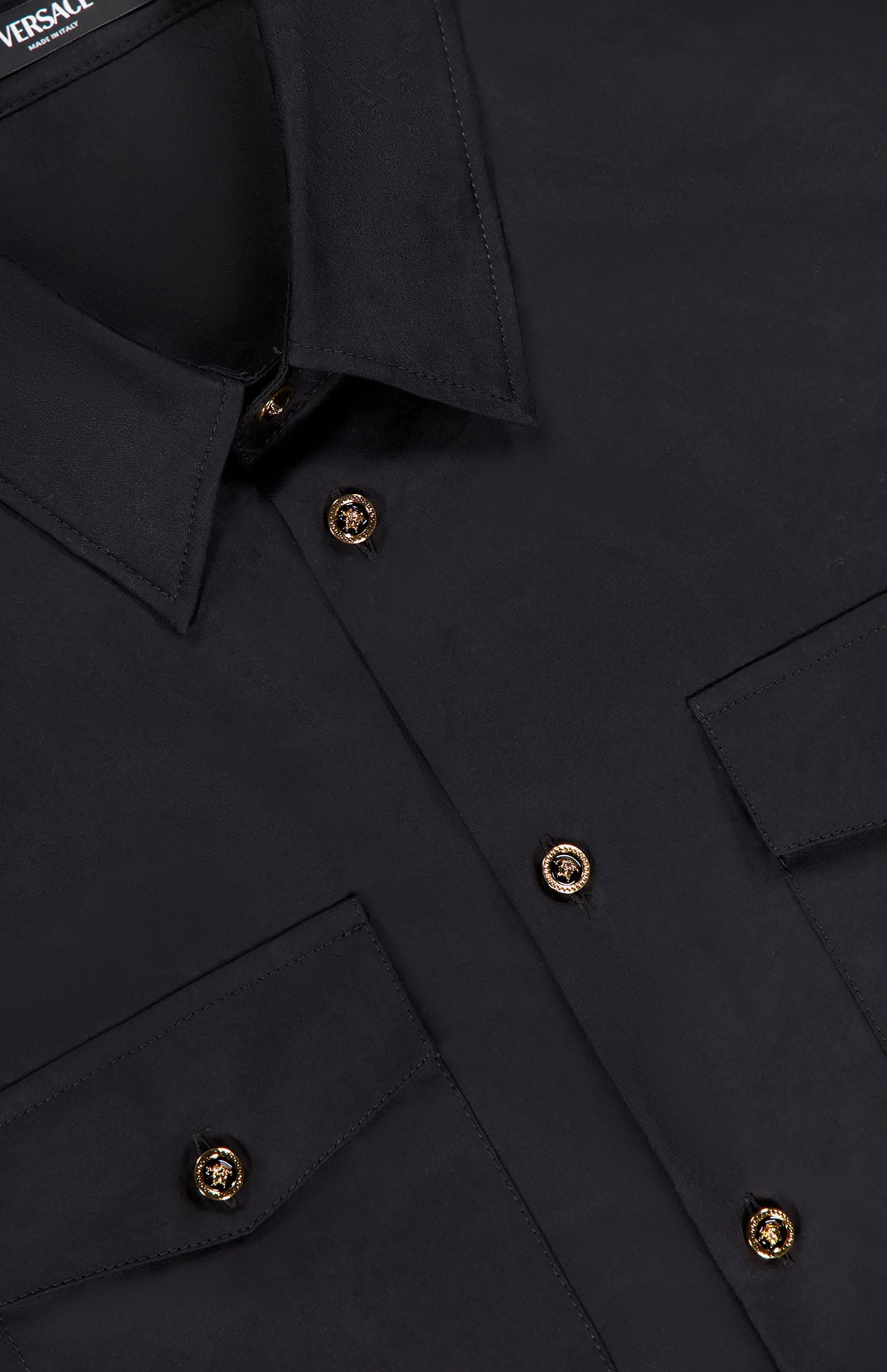 Close-up of the black VERSACE Baroque Jacquard Poplin Shirt with gold Medusa buttons, two flap chest pockets, fine stitching, and signature Barocco pattern accents emphasizing its luxurious details.