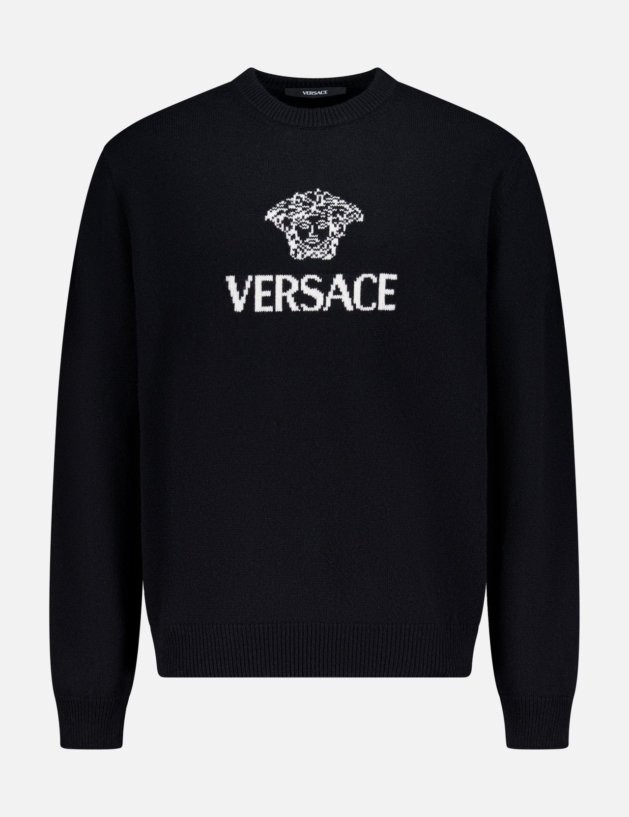 The Medusa Cashmere Knit Sweater by VERSACE is a black crewneck with long sleeves, showcasing the iconic Medusa logo and bold white VERSACE branding on the front—a standout in luxury Italian menswear.